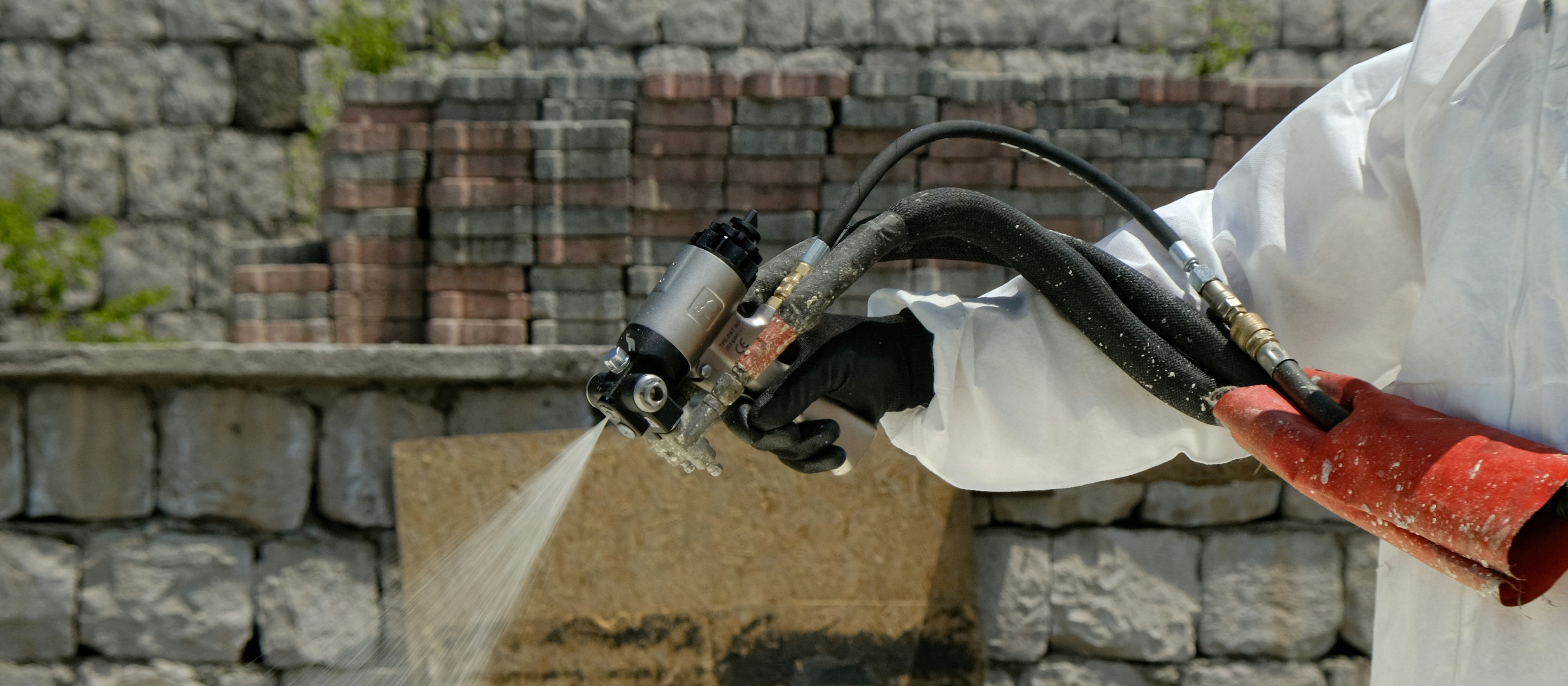Applicator in white protective coverall firing a plural-component spray gun, polyurethane foam leaving the nozzle